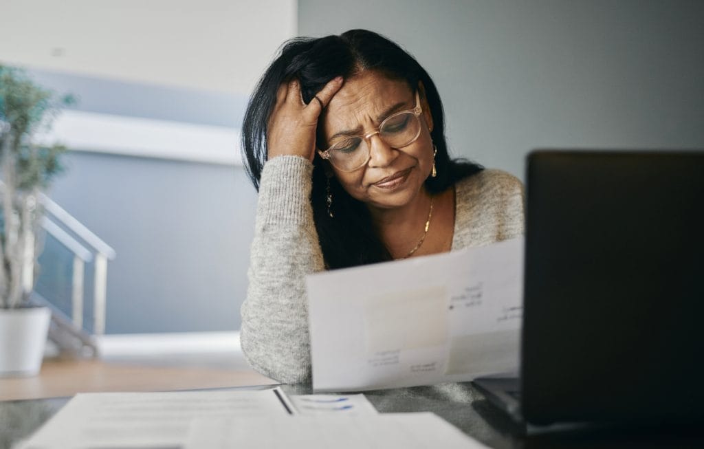 Retired woman sat at a desk looking stressed whilst holding bills, finding a way to clear debt in retirement